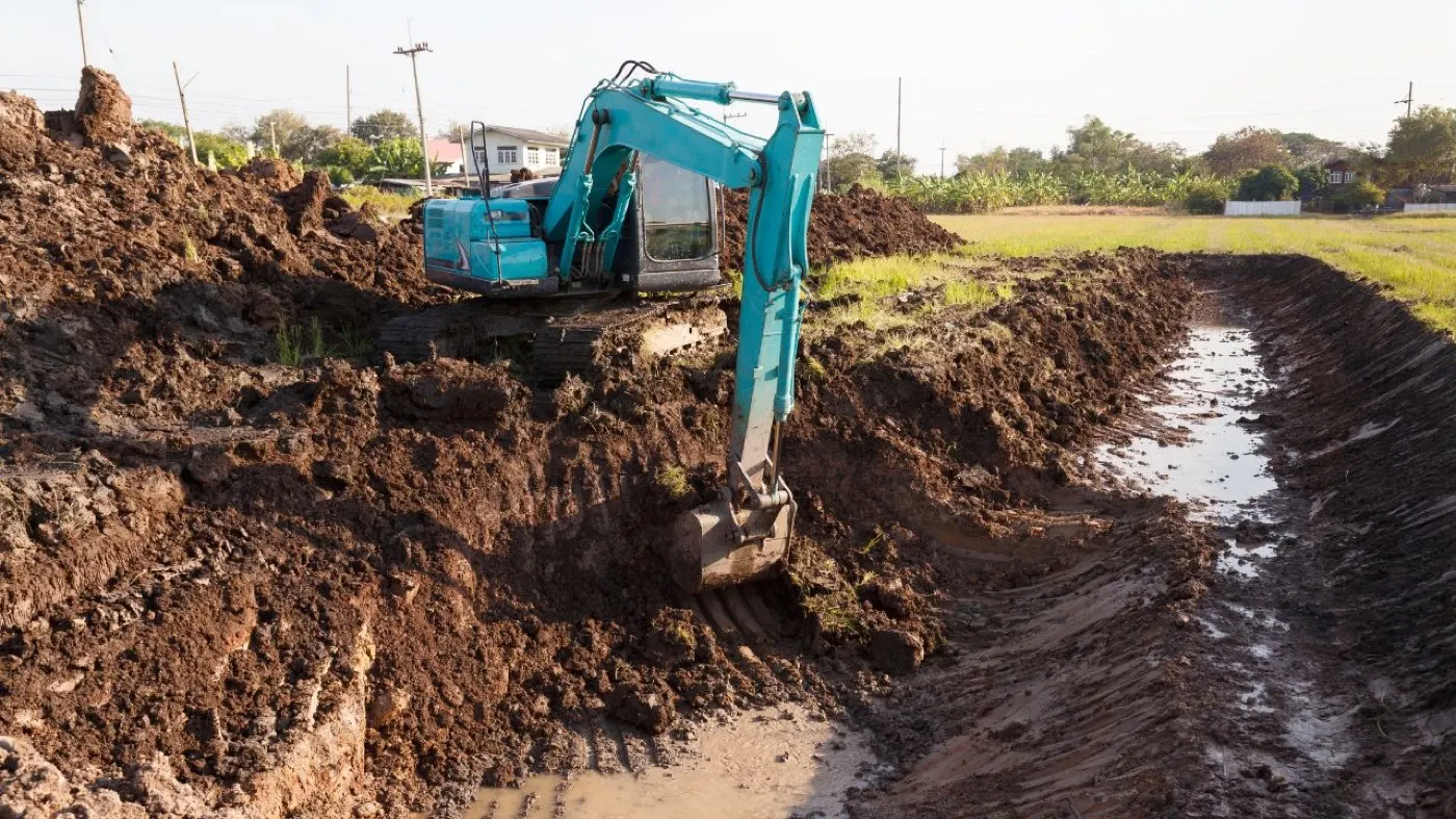 Excavator cutting a drainage channel through wet clay soil